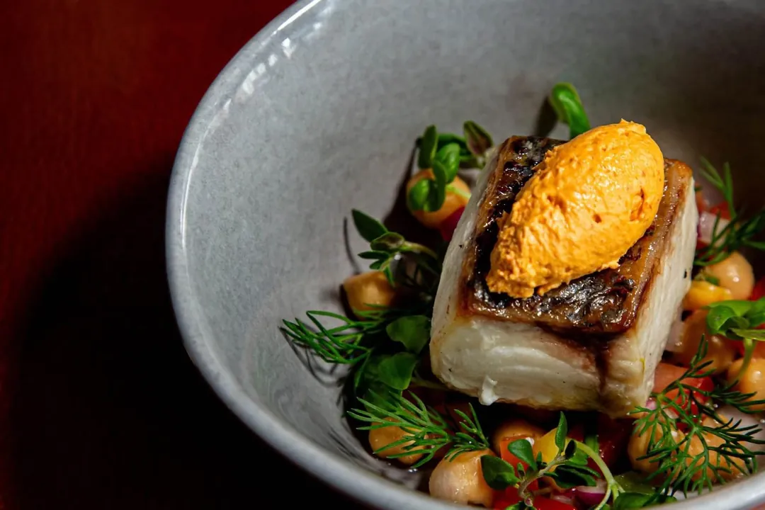 A fillet of white fish with a quenelle of orange purée, chickpeas and fresh herbs
