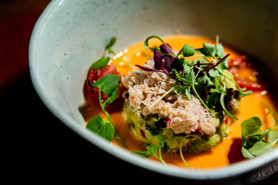 Crab over a bright orange sauce with herbs, in a bowl