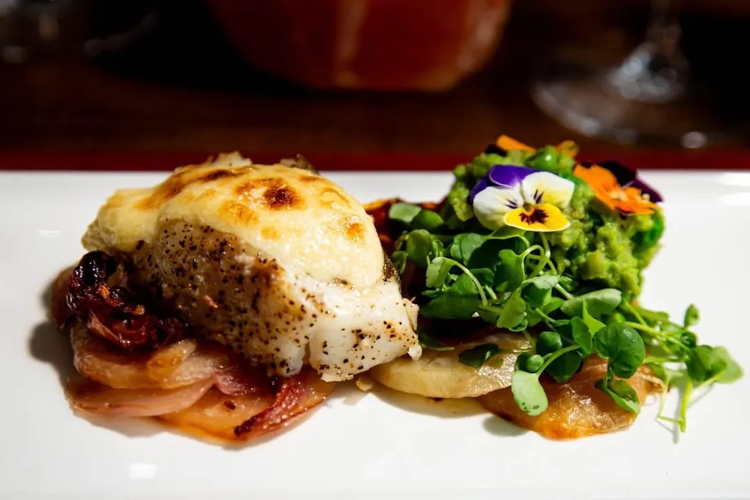 A baked fillet with greens and edible flowers on a white plate