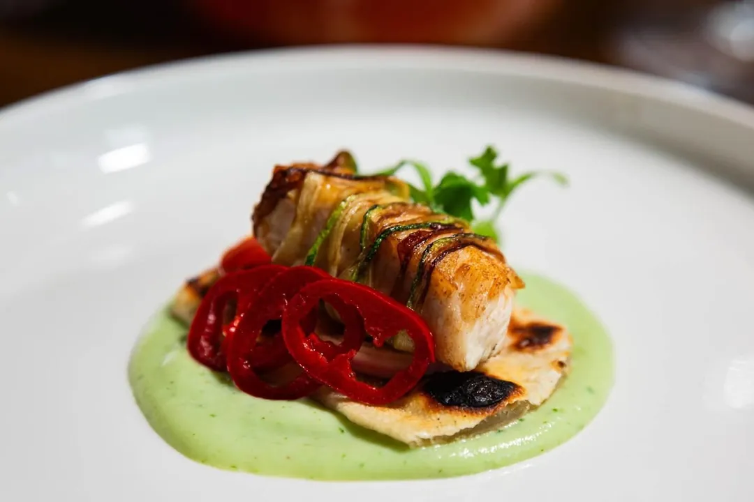 Grilled fish on a green herb purée with charred red peppers
