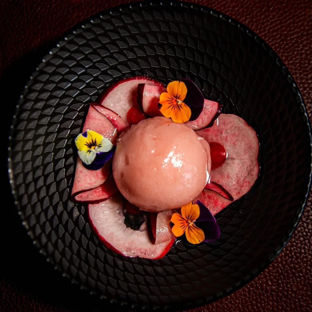 A pink dessert decorated with edible flowers, in a black bowl